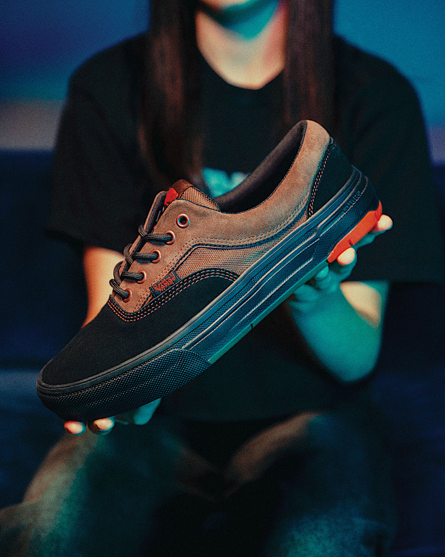 Person holding a brown and black sneaker against a dark background