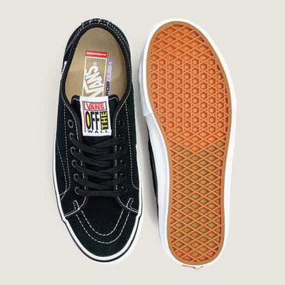 A pair of Vans Off-White low-top sneakers shown from a top-down view, with one shoe displaying the black suede and canvas upper, white laces, and white Vans logo tab, and the other shoe showing the textured brown gum outsole.