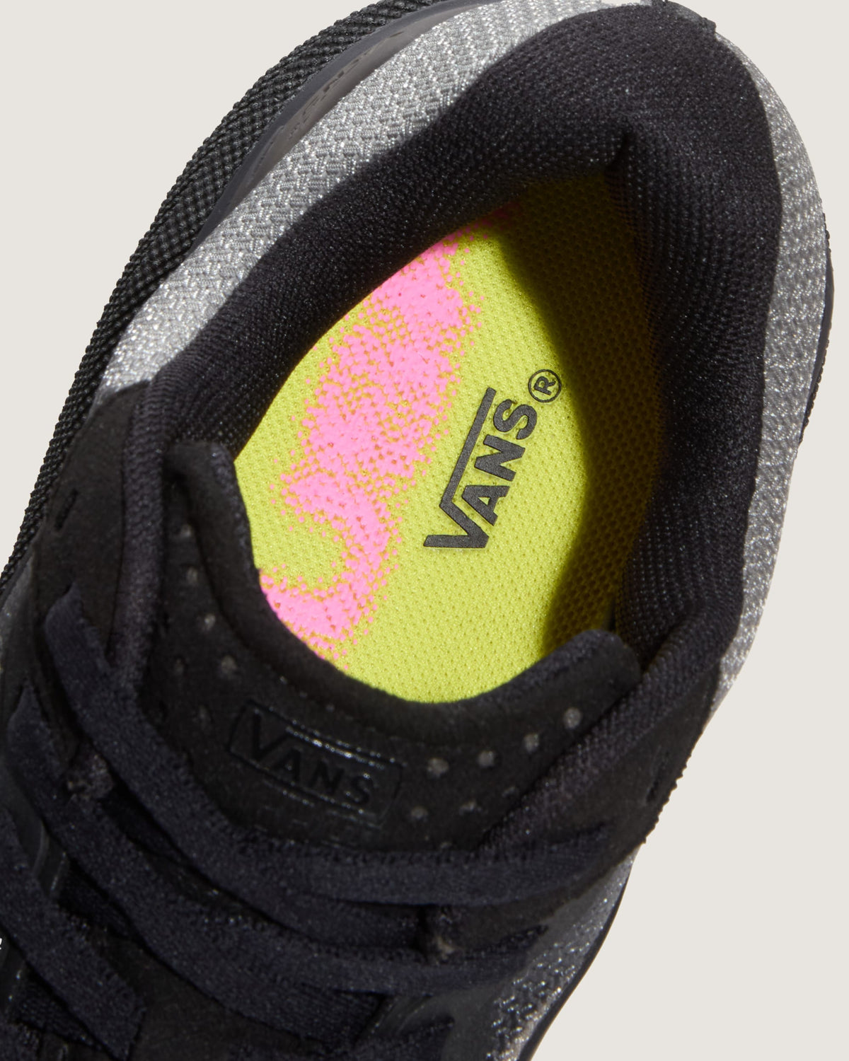 Close-up of a Vans sneaker showing the black mesh upper, gray knit collar, and a bright neon yellow-green insole with a pink Vans logo.