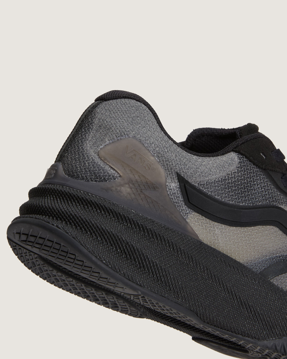 Close-up of the side and heel of a black and gray running shoe, showing the textured mesh upper, translucent side panel, and thick black sole against a light gray background.
