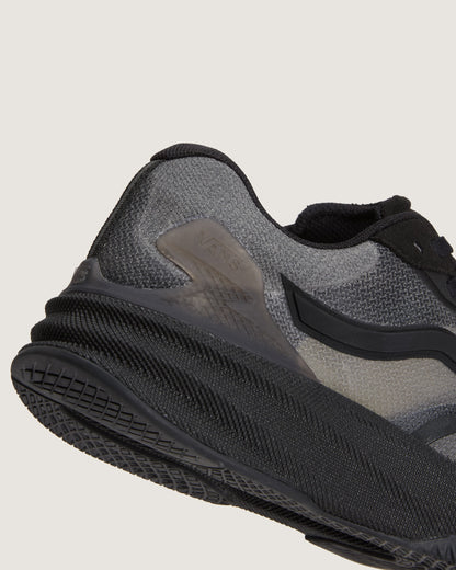 Close-up of the side and heel of a black and gray running shoe, showing the textured mesh upper, translucent side panel, and thick black sole against a light gray background.