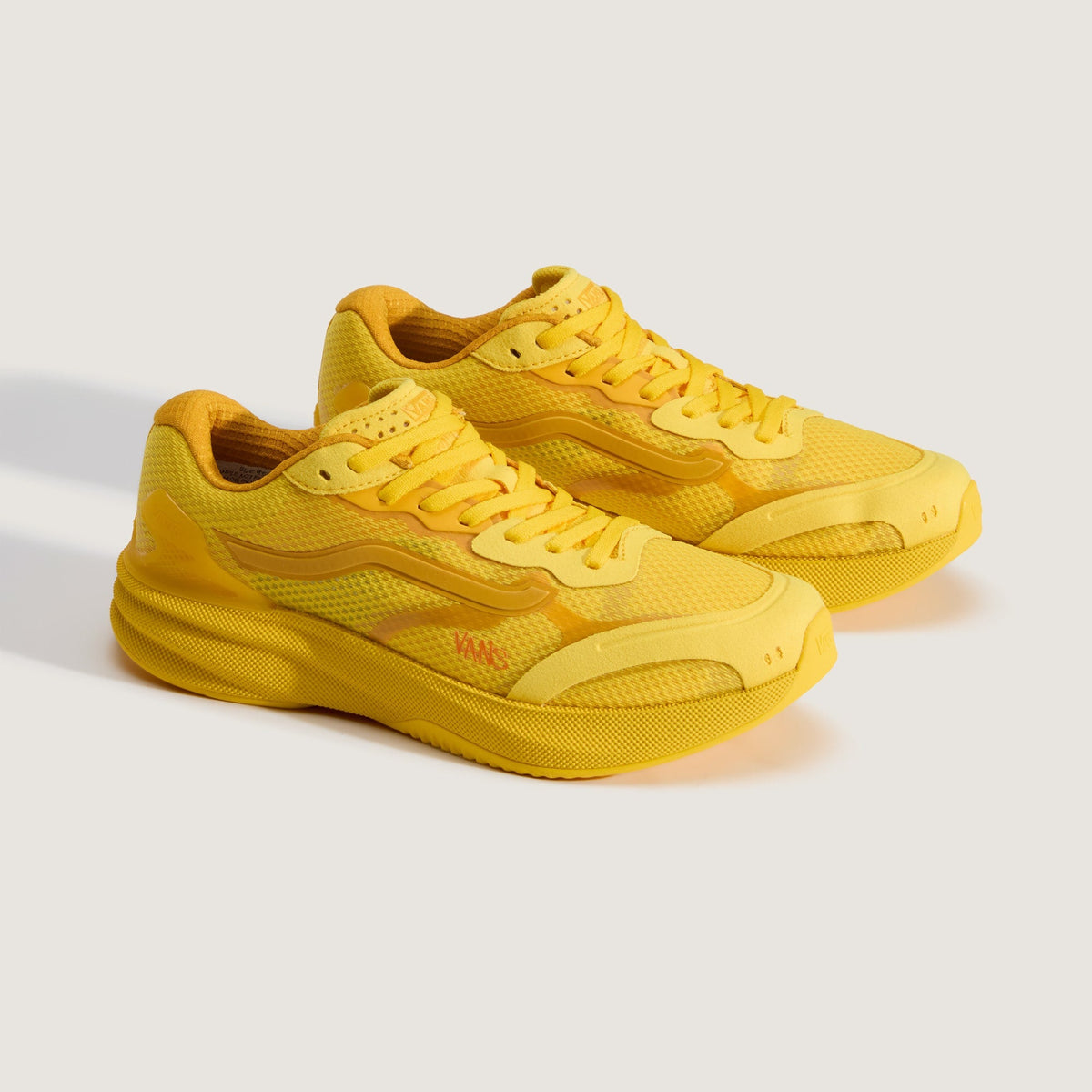 A pair of yellow athletic sneakers with a mesh upper and thick sculpted sole, photographed on a clean light gray studio background.