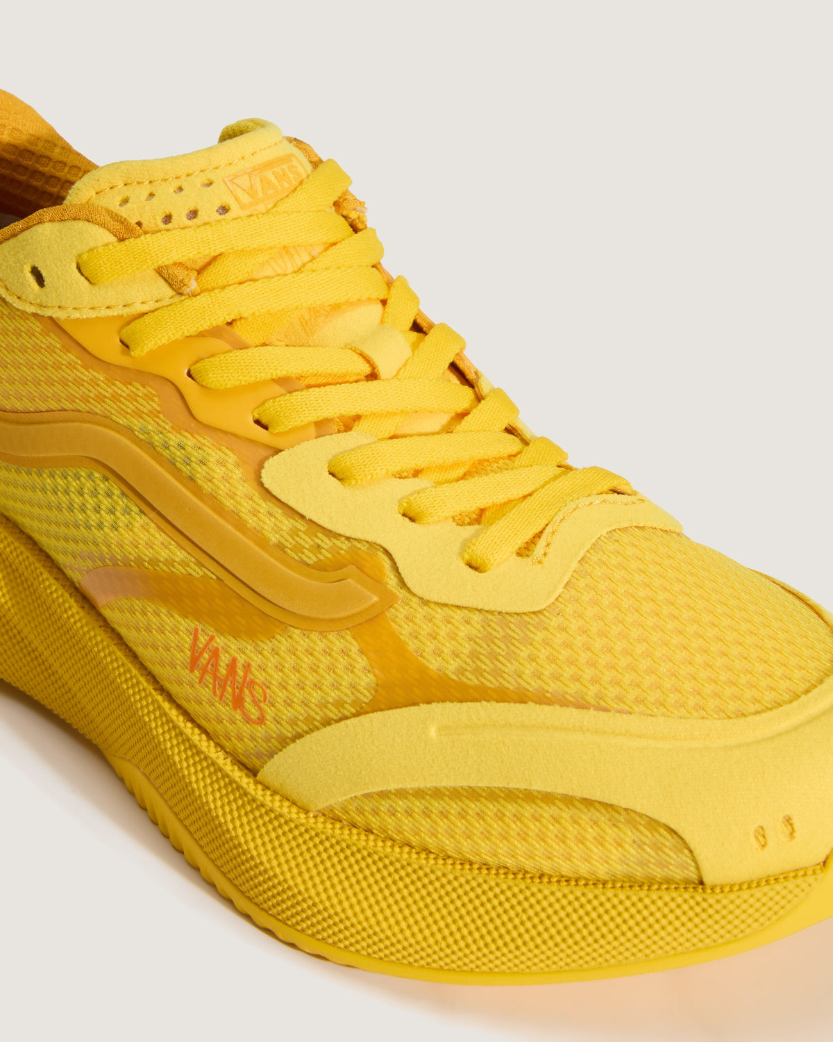 A close-up of a yellow Vans sneaker showing the side profile, mesh upper, laces, and textured sole on a light gray background.