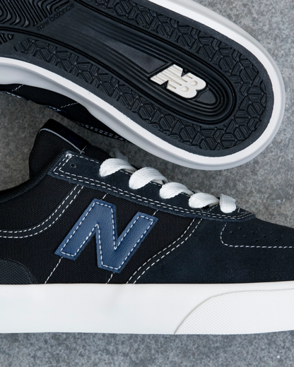 Black sneaker with white laces and sole on a gray surface