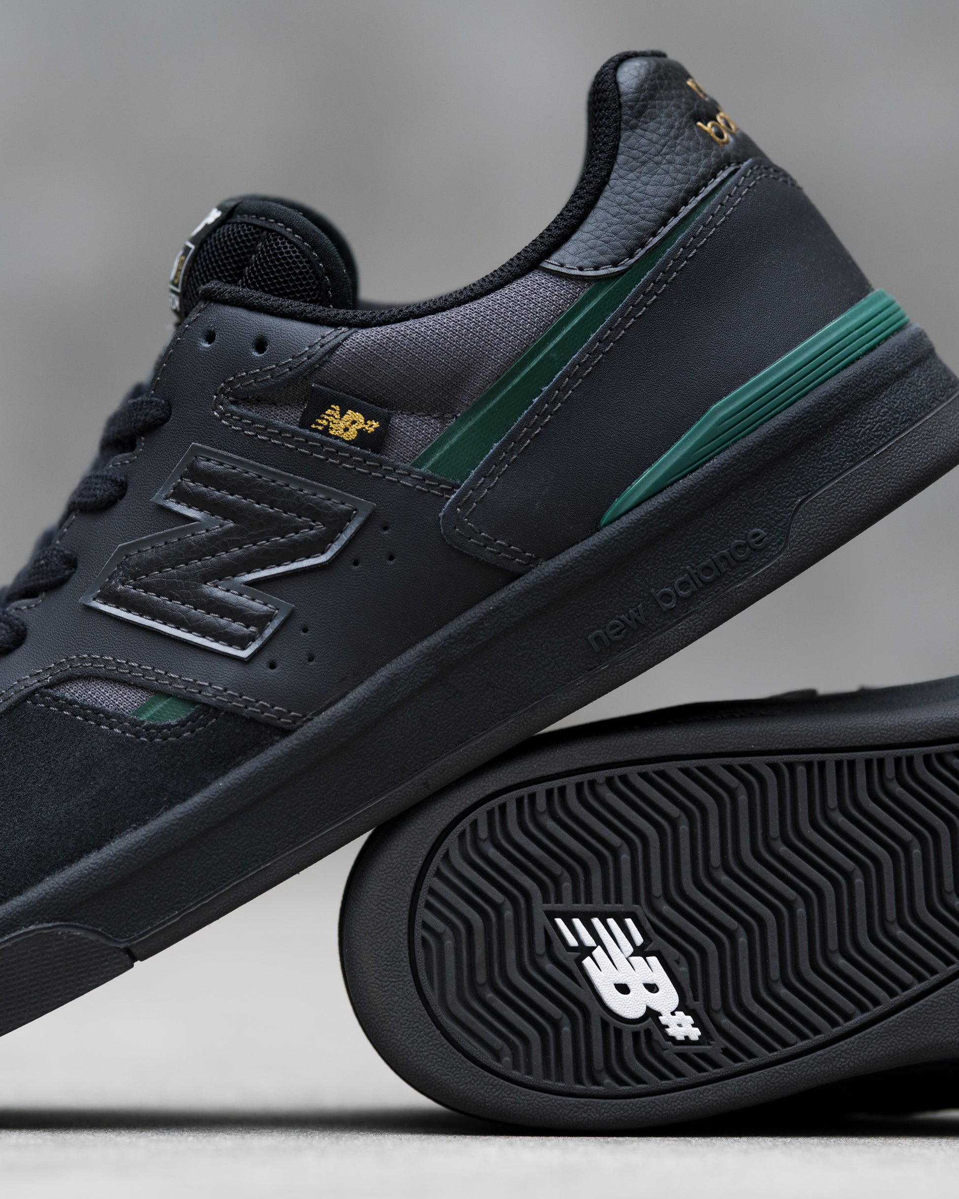 Black New Balance sneaker with green accents on a gray background