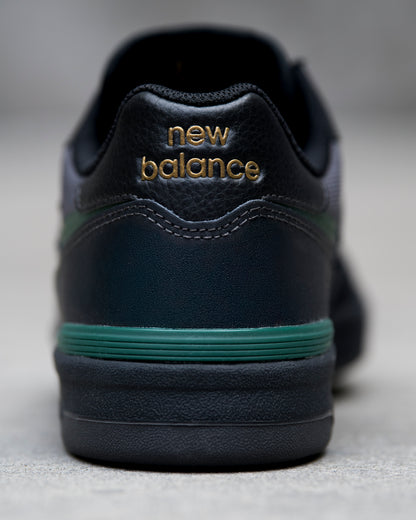 Black New Balance sneaker with green sole on a light gray background