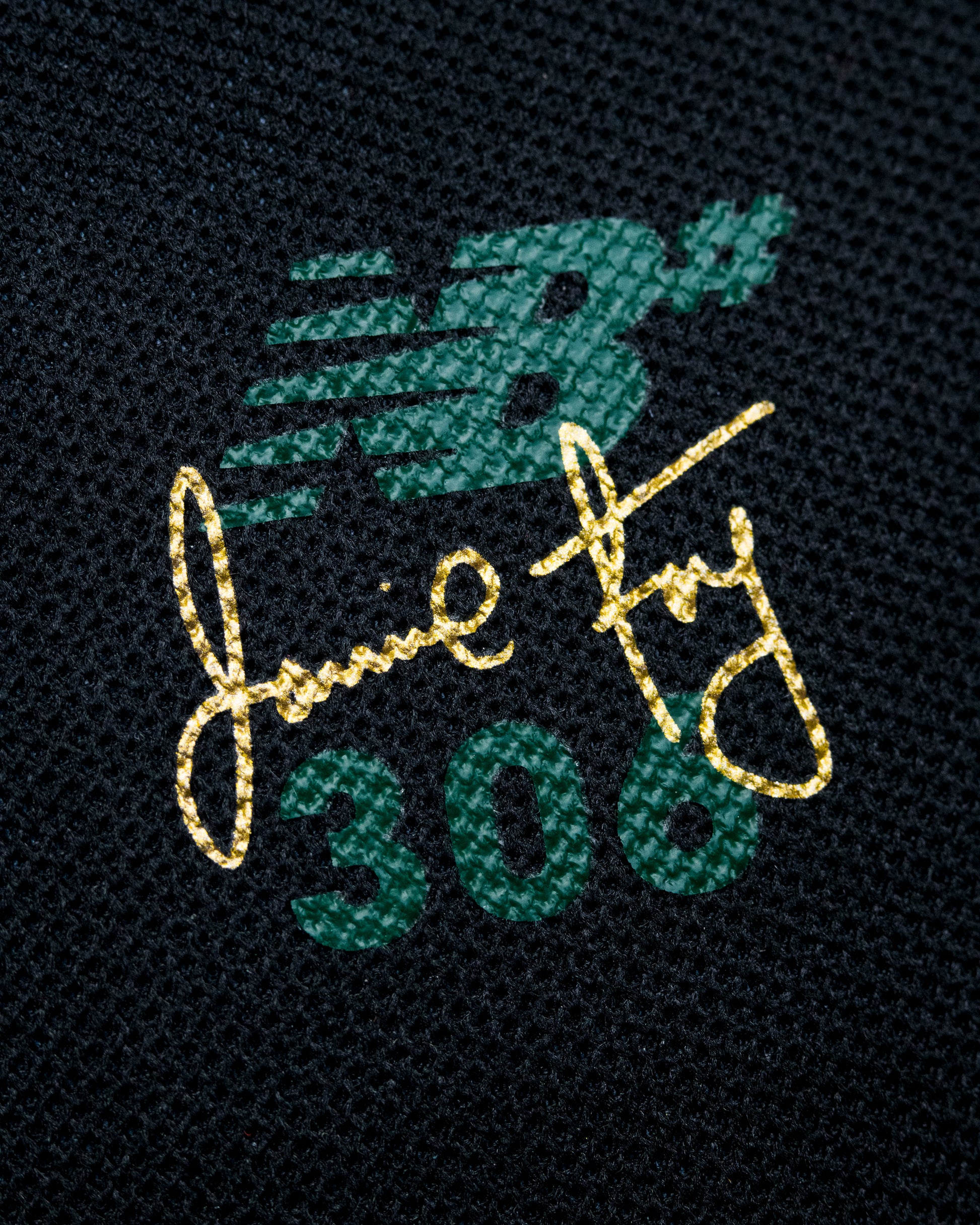 Embroidered design on a dark fabric background with gold and green text and logo.