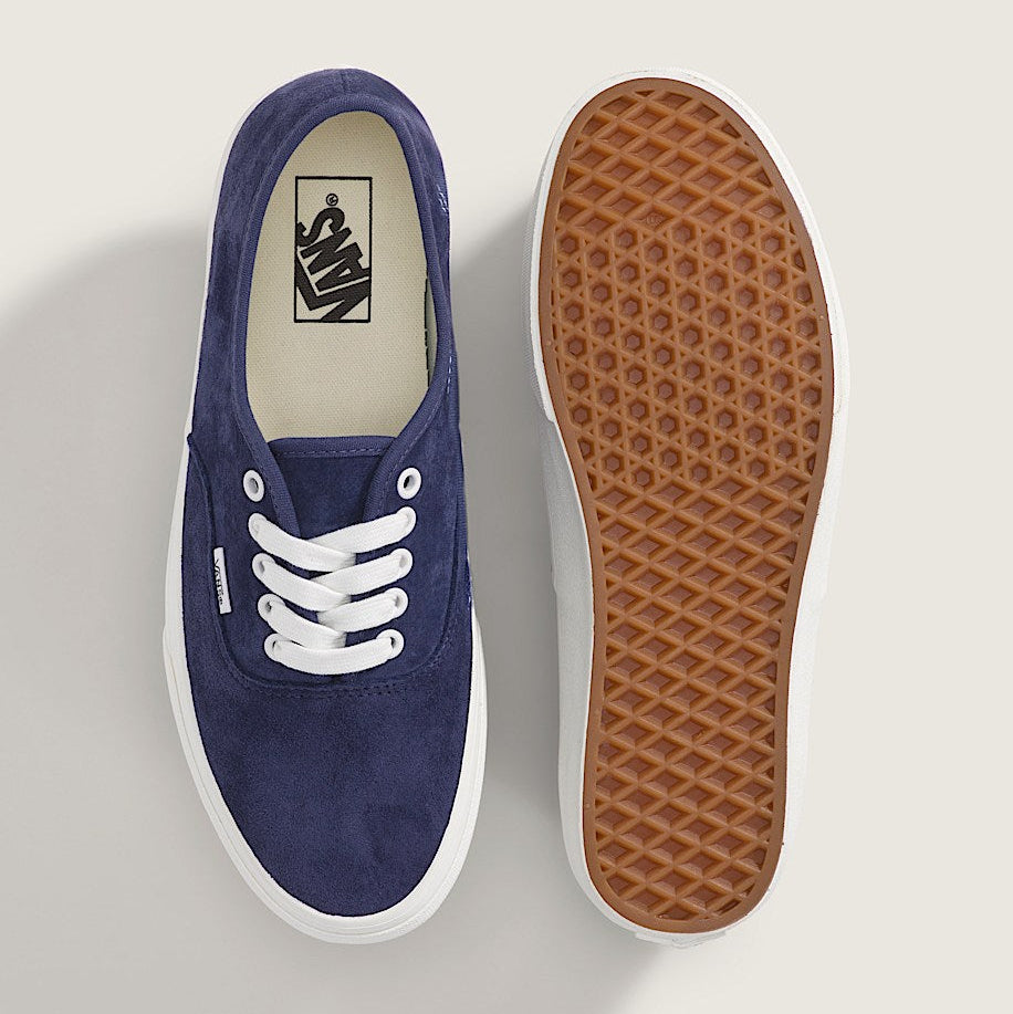 Navy blue sneaker with white laces and brown sole on a light gray background