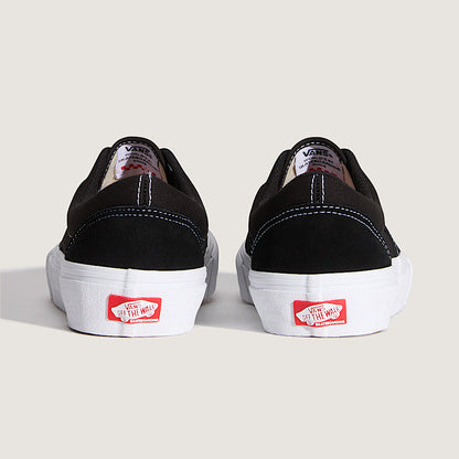 Black sneakers with white soles and red Vans logo on a light beige background