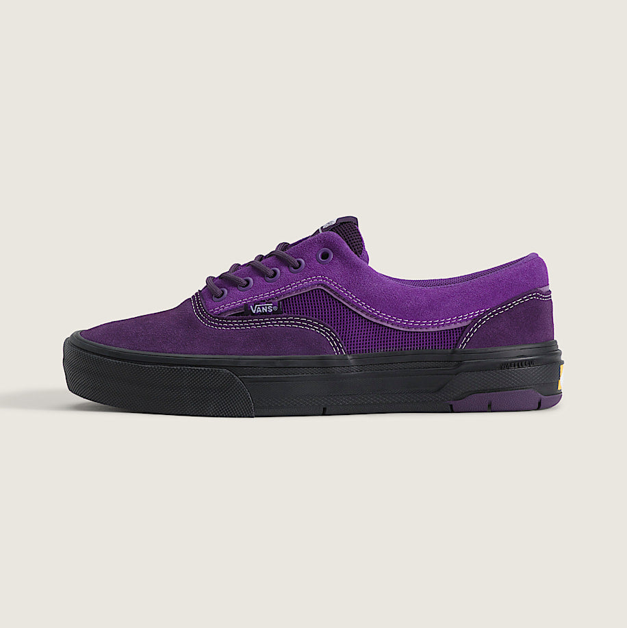 A purple suede and canvas low-top sneaker with black laces and a black rubber sole, shown in profile against a light beige background.