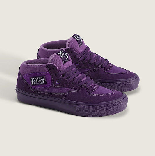 A pair of purple suede and canvas mid-top skate shoes with matching purple soles, displayed on a light beige background. The shoes feature a side logo patch that reads 'Fate University' and a tongue label with 'Vans' and 'Skate'.