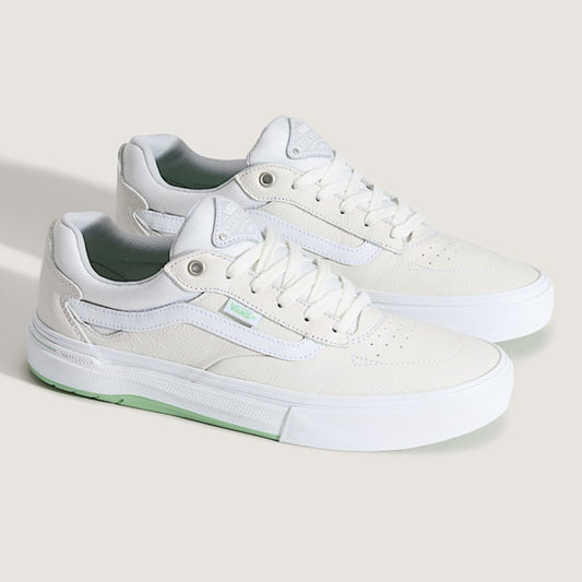 White sneakers with green accents on a light beige background