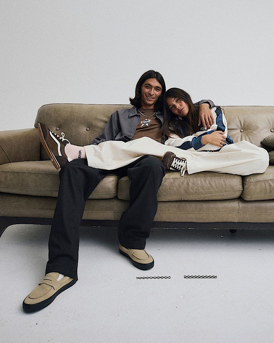 Two people sitting on a couch with a guitar, wearing casual clothing.