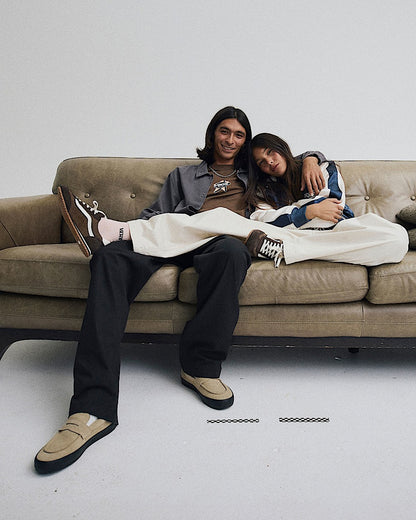 Two people sitting on a couch with a guitar, wearing casual clothing.