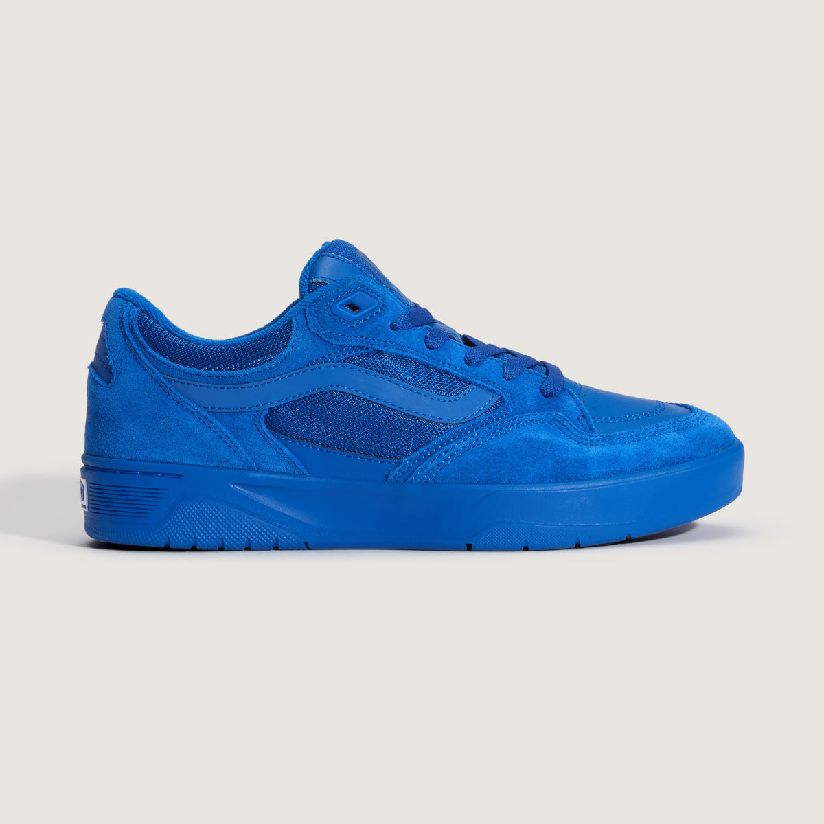 A low-top sneaker in a solid vibrant blue color, featuring suede and mesh panels, laces, and a thick platform sole, shown from a side profile on a light beige background.