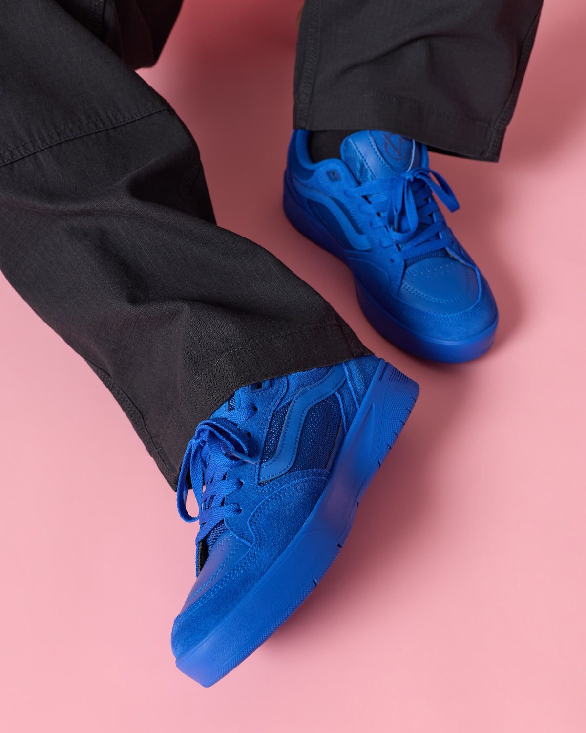 A pair of bright royal blue low-top sneakers worn with black pants against a solid pink background.