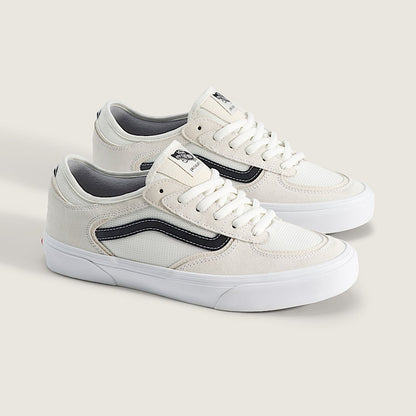 A pair of low-top Vans sneakers in off-white canvas with dark navy side stripes and white laces, displayed on a light beige background.