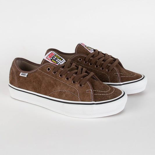 A pair of brown suede low-top sneakers with white rubber soles, featuring a black stripe and a colorful Vans logo patch on the side.