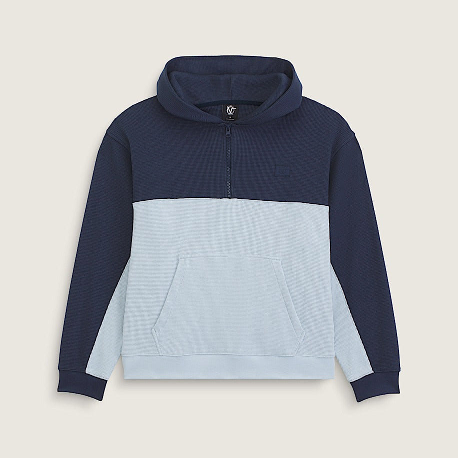 A color-blocked pullover hoodie with a navy blue upper section and sleeves, a light blue lower body, and a light blue front pocket, shown on a neutral beige background.