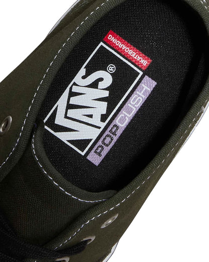 Close-up of the inner side of a Vans low-top shoe, showing the black fabric lining with the large white Vans logo, a red Skateboarding label, and a lavender Pop Cush label, on a light beige background.